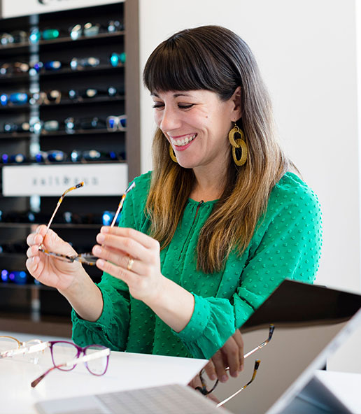 Woman smiling while trying on designer eyeglasses at Vision Specialists